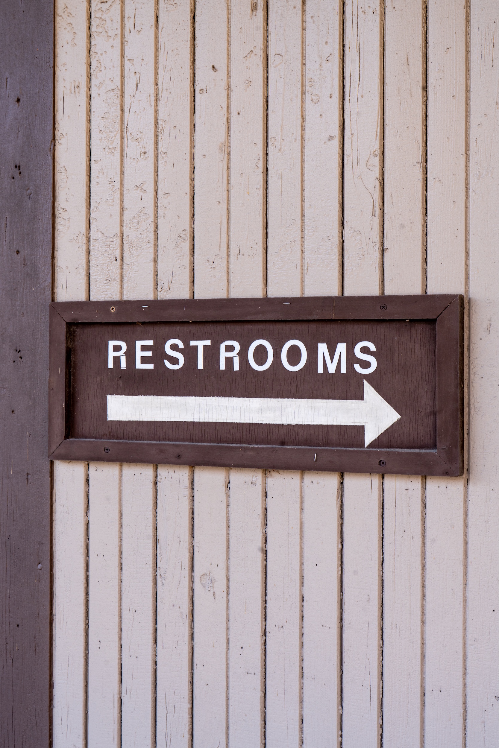 A restrooms directional sign on a wall at a park.